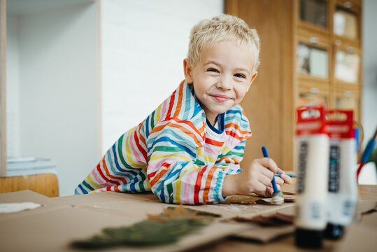 Little blonde boy playing with paint and autumn leafs