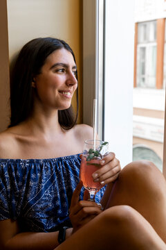 Portrait of young woman having a drink sitting next to window