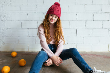 Girl in warm clothes sitting near brick wall