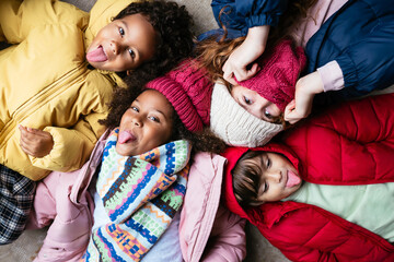 Cute multiethnic kids in warm clothes relaxing on floor