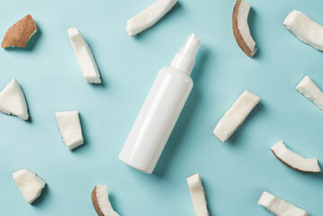 Top view photo of natural care product in white bottle with copyspace on isolated blue background with pieces of fresh coconut