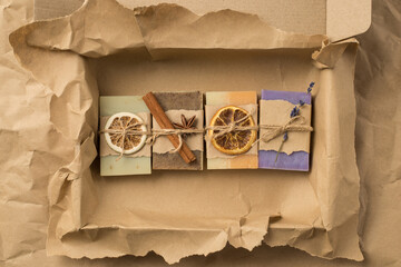 Top view photo of organic solid care products with dried citrus slices lavender cinnamon lying in row in cardboard box on crumpled craft paper background