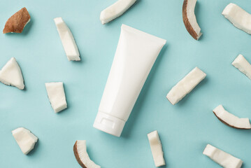 Top view photo of organic care product in white tube with copyspace on isolated blue background with pieces of fresh coconut