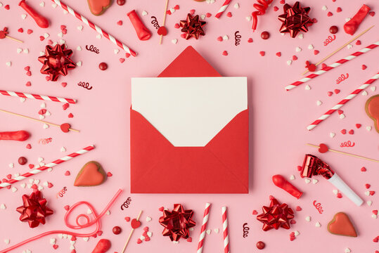 Top view photo of birthday composition with red ribbon stars serpentine confetti heart-shaped cookies bright decorations and red open envelope with copyspace in the middle on pastel pink background - Powered by Adobe