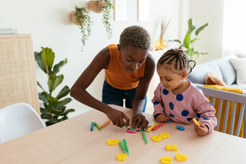 Black mother helping daughter to created modeling clay figures