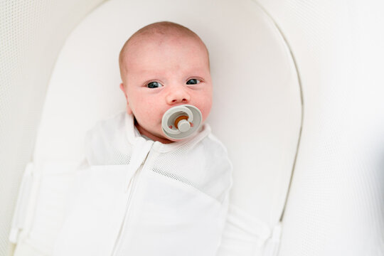 Newborn with pacifier in white bassinette