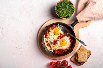 Flat lay image of shakshouka in a pan on a light coloured background