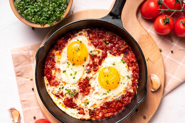Flat lay image of shakshouka in a pan on a light coloured background