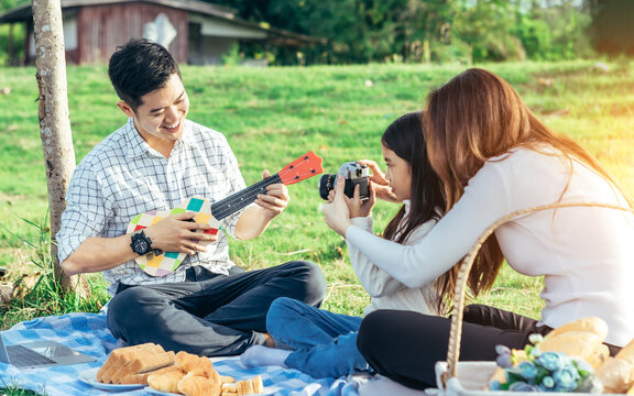 Happy asian family in the garden They play ukulele, singing, take pictures by film camera, eat together and have fun.