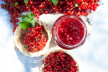 Red and ripe red currants in a straw bowl  and jars of berry jam, flat lay. Harvest and cooking theme