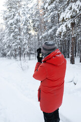 A man in a red jacket with a camera in rukh takes pictures of a winter forest