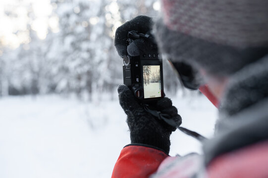 A man in a red jacket with a camera in rukh takes pictures of a winter forest