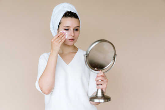 Woman with mirror using cotton pad for skincare procedure