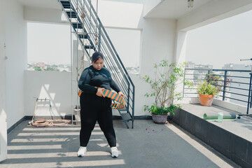 Plus size young asian woman playing hula hoop in balcony. Helps to burn excess fat in body. Strengthens the muscles of the body, going to loose extra pounds at home,