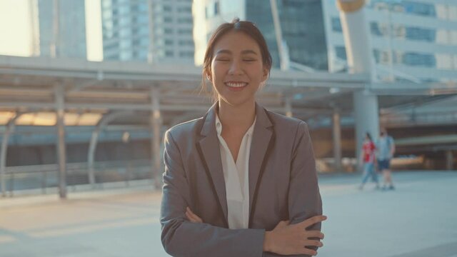 Successful young Asia businesswoman in fashion office clothes smiling and looking at camera while happy standing alone outdoors in urban modern city in the morning. Business on the go concept.