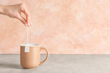 Woman dipping tea bag into cup on color background