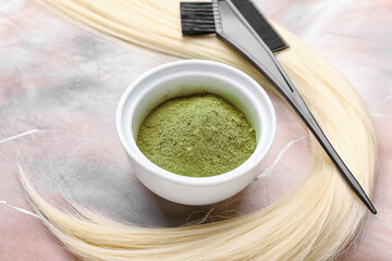 Bowl with henna, hair and comb on color background, closeup