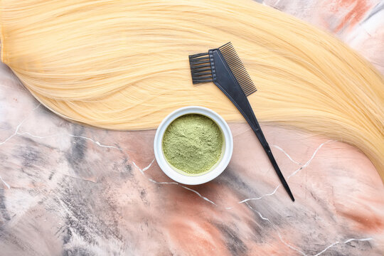 Bowl with henna, hair and comb  on color background