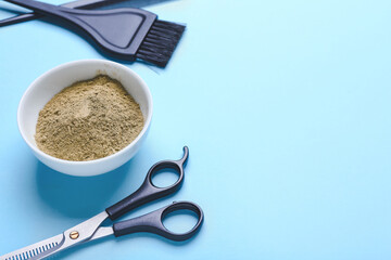 Bowl with henna and hairdresser's supplies on color background
