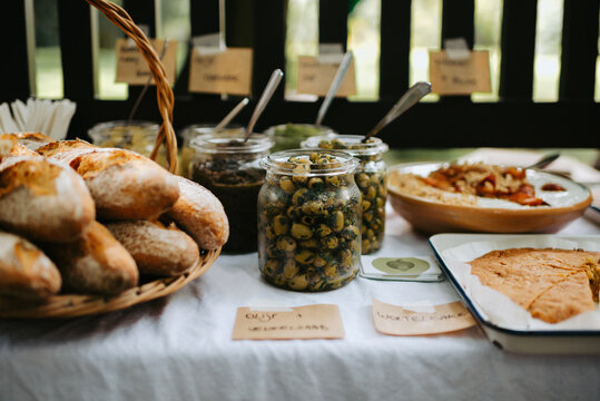 Outdoor table with french baguettes in a basket, olives and other spreads and cake