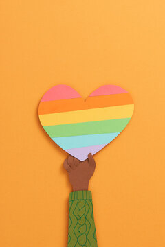 Human hands holding heart with rainbow flag as a symbol of LGBT isolated over orange background