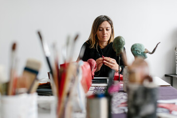 Female sculptor modeling on wax sitting on a table in her workshop