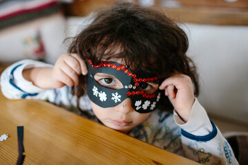 Kid covering her face with a decorated cardboard mask looking at camera