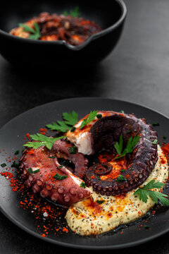 Grilled Octopus with hummus and spices on a dark background
