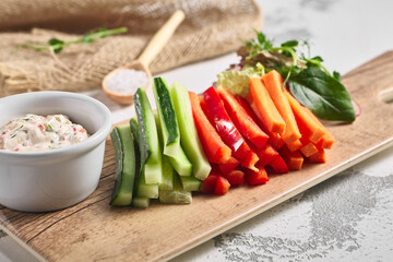 Fresh vegetable food platter on white table. Slices vegetable on wooden board with dip sauce. Rustic food concept.