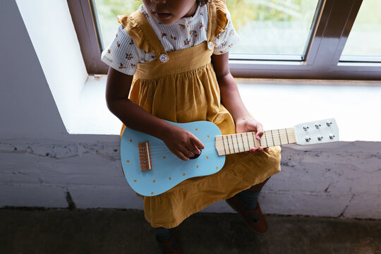 Black child playing ukulele near window