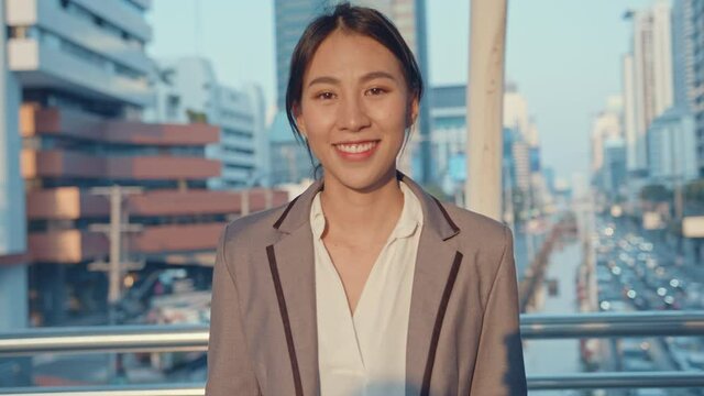 Successful young Asia businesswoman in fashion office clothes wear medical face mask smiling and looking at camera while happy standing alone outdoors in urban modern city. Business on the go concept.