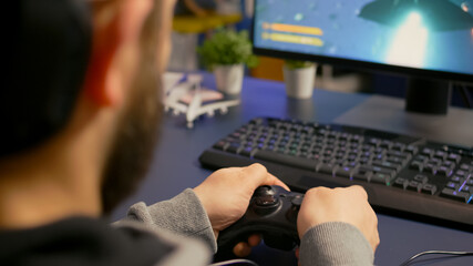 Close-up of gamer playing first person online competition using professional wireless controller. Pro player use joypad for digital championship sitting on gamining chair late at night in living room © DC Studio