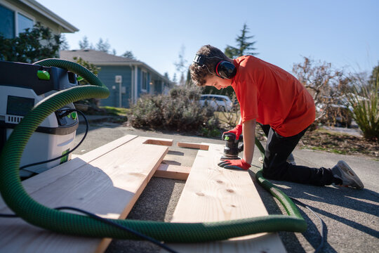 Young boy sands a board in driveway. - Powered by Adobe