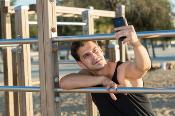 Cheerful sporty man taking selfie on beach fitness station