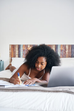 Black teenager doing homework on bed