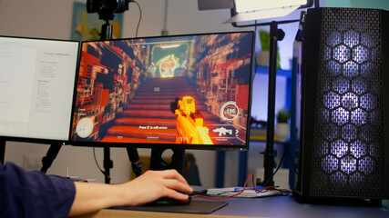 Close-up of streamer playing first person shooter video game using RGB keyboard and mouse. Gamer talking on streaming chat with other players during esport tournament late at night in gaming studio
