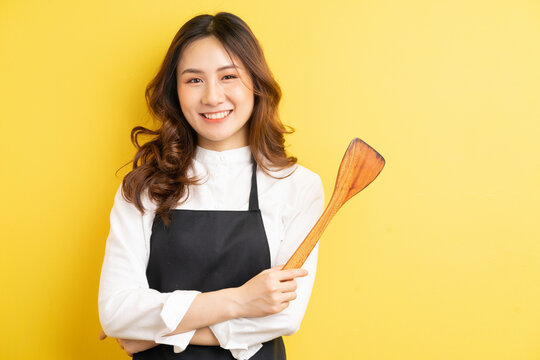Housewife beauty holding rice spoon and smile isolated on yellow background