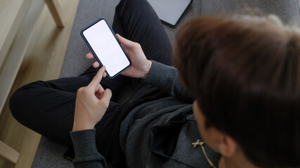 Overhead shot of casual man sitting on sofa with crossed legs and using mobile phone.