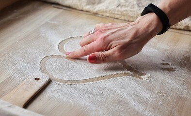 a woman's hand draws a heart on flour scattered on the work surface in a home kitchen