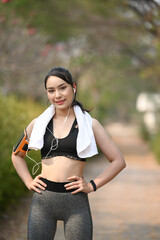 Portrait of sporty woman with white towel smiling to camera and standing in the public park.