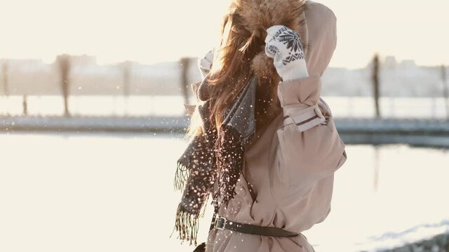 Winter girl portrait. Beauty joyful model girl blowing snow, having fun in winter park. Beautiful young woman enjoying nature outdoors. Wintertime.