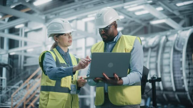 Team of Diverse Professional Heavy Industry Engineers Wearing Safety Uniform and Hard Hats Working on Laptop Computer