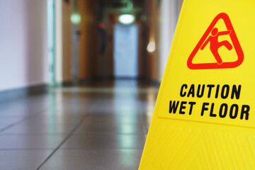 A sign that reads Caution is a long empty industrial corridor. Yellow sign of slippery floor in the...