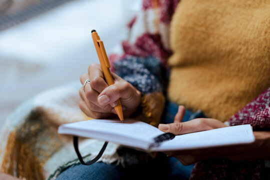 Woman in a cafe, writing on her book note some ideas, while drin