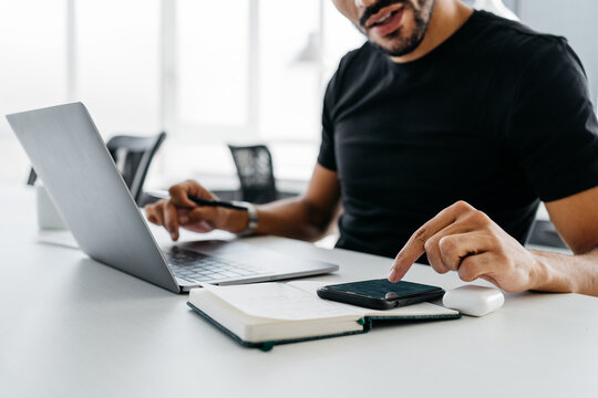 Anonymous crop man checking his smartphone while he is working with his laptop
