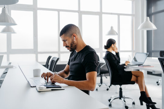 Side view of arab man and unrecognizable woman working on their laptops in a modern and bright coworking
