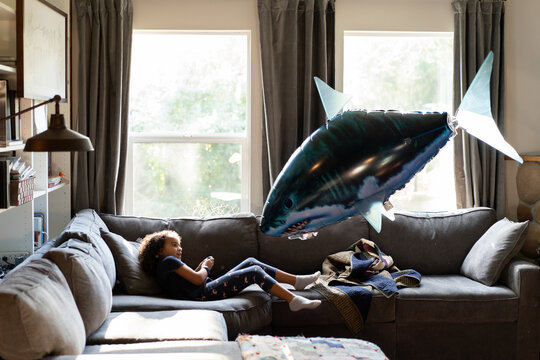 Girl on couch under flying balloons shark