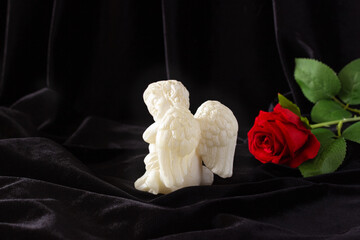 A little angel with wings and a red rose on a black background. Funeral concept, condolences