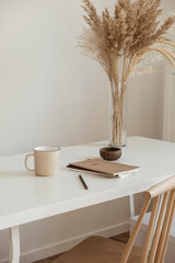 Aesthetic minimal office workspace interior design. Mug, notebook, pampas grass floral bouquet on...