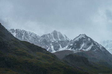 Atmospheric alpine landscape with great mountain peaked top with snow in low clouds. Dramatic mountain scenery with sharp pinnacle in overcast weather. Awesome view to snowy pointy peak in cloudy sky.